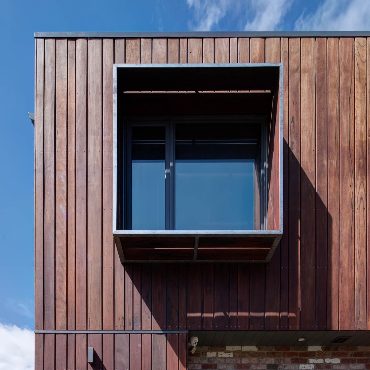 Timber-clad rear addition with a projecting box window against a blue sky